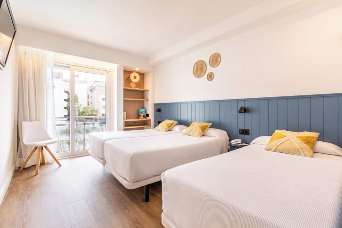 A hotel room with two beds, a small seating area, a balcony, and a wall with decorative plates.