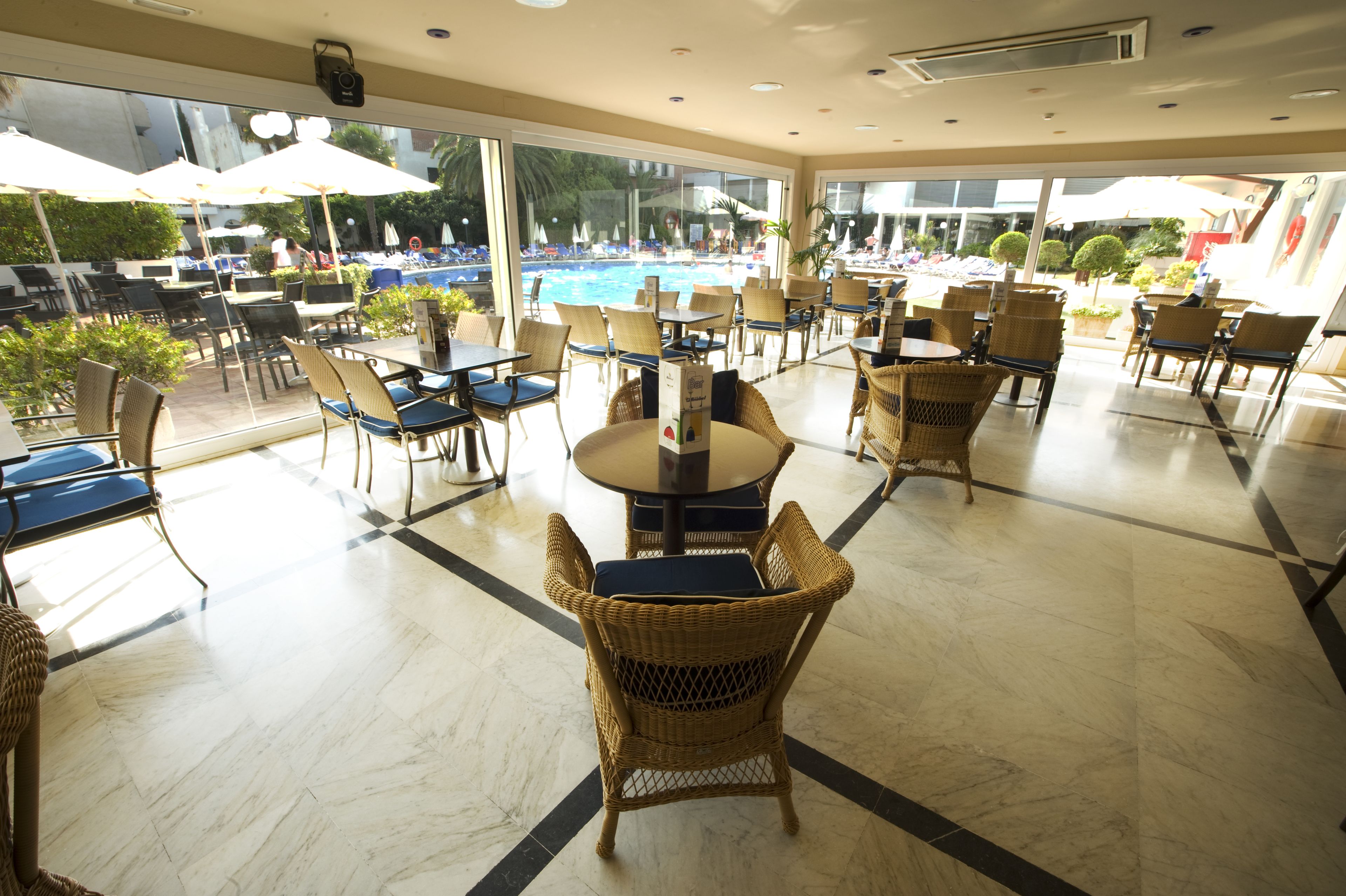 A spacious indoor area with tables and chairs, large windows, and a pool visible through the glass.