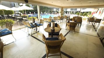 A spacious indoor area with tables and chairs, large windows, and a pool visible through the glass.