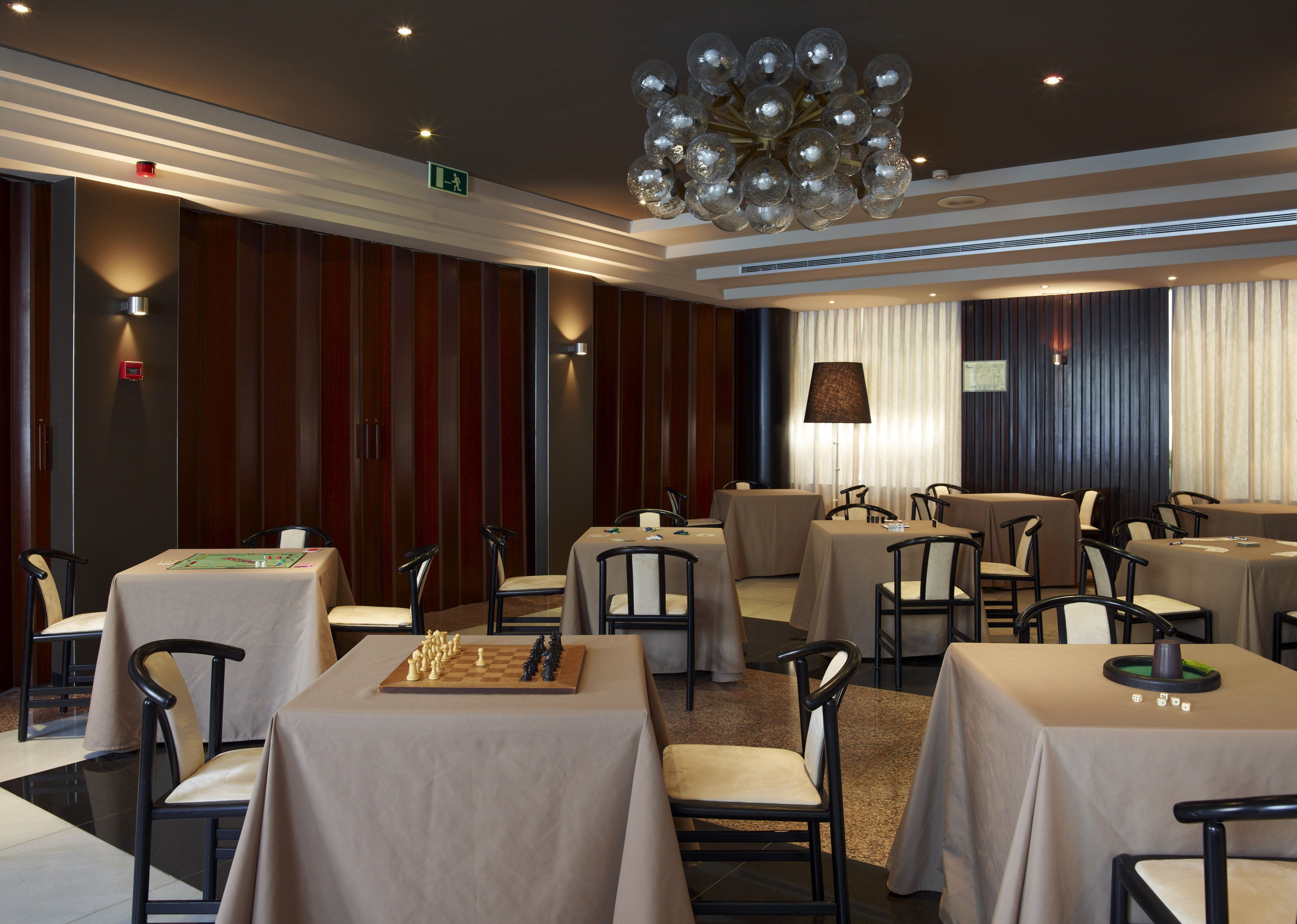 A hotel dining area with multiple tables and chairs, a chandelier, and a chessboard on one table.