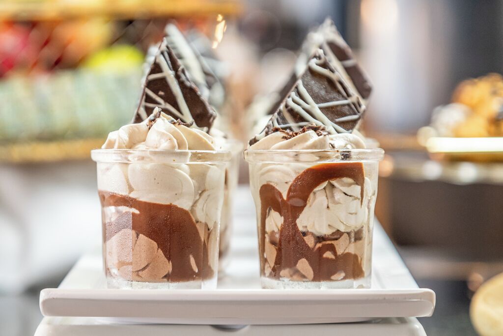 Dos vasos de postre amb nata i salsa de xocolata, decorats amb un reg de xocolata.
