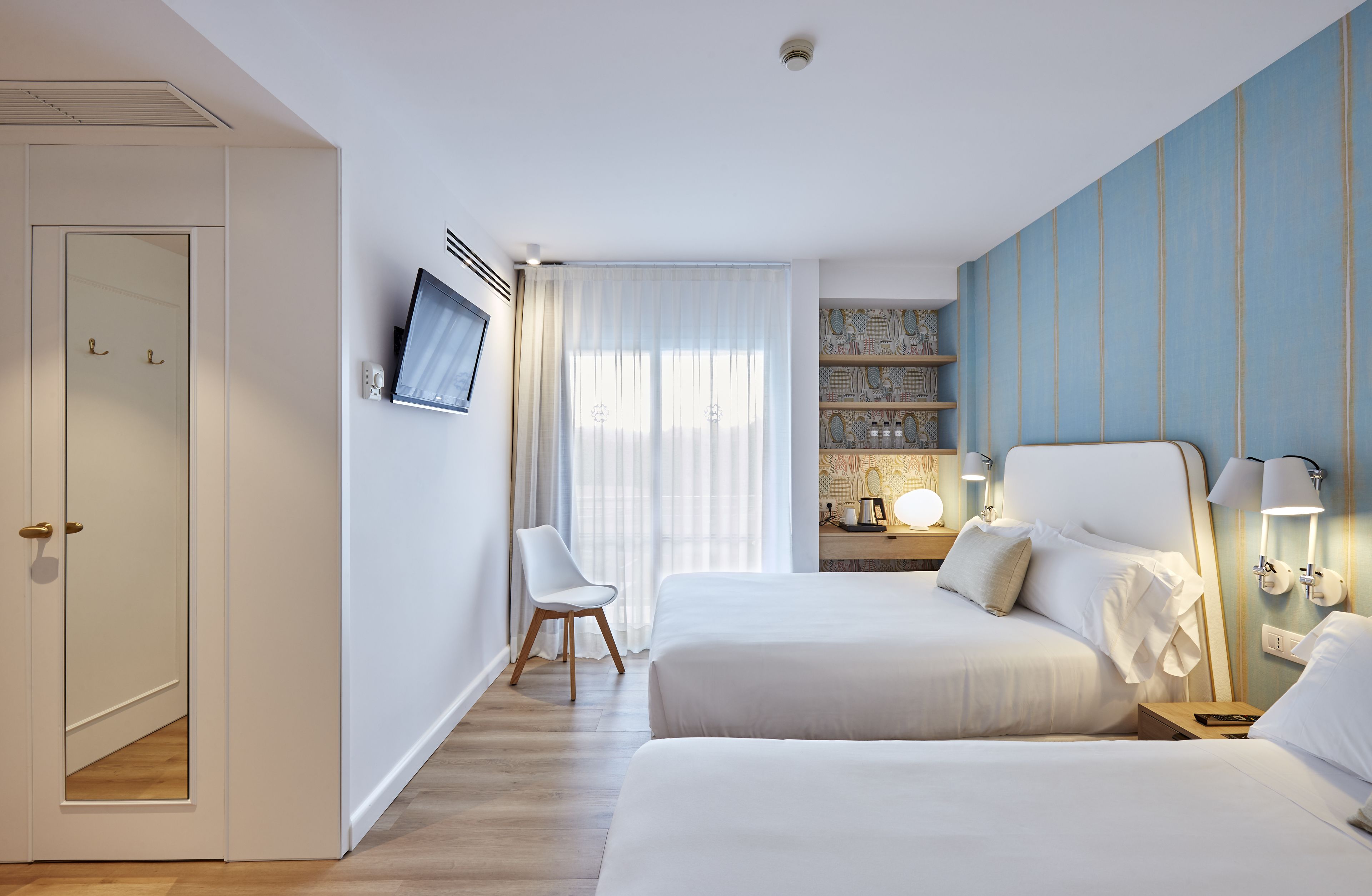 Habitación de hotel con dos camas, un televisor, un escritorio con lámpara y una estantería.