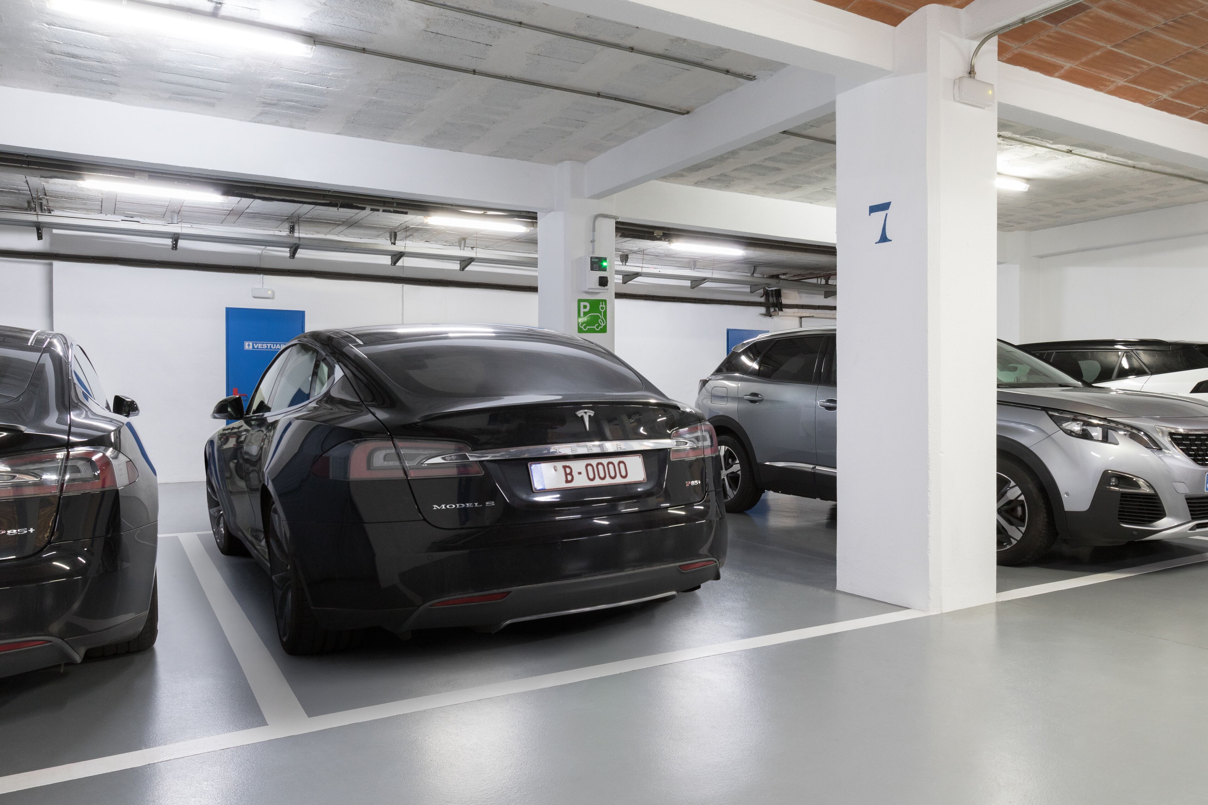 A parking garage with multiple cars, including a black Tesla Model S.
