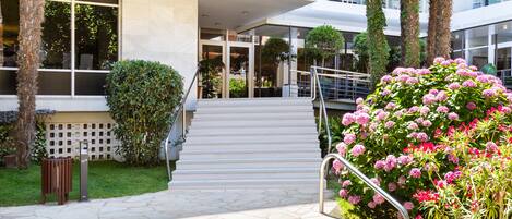 A hotel entrance with a staircase leading to the lobby, surrounded by lush greenery and a well-maintained garden.