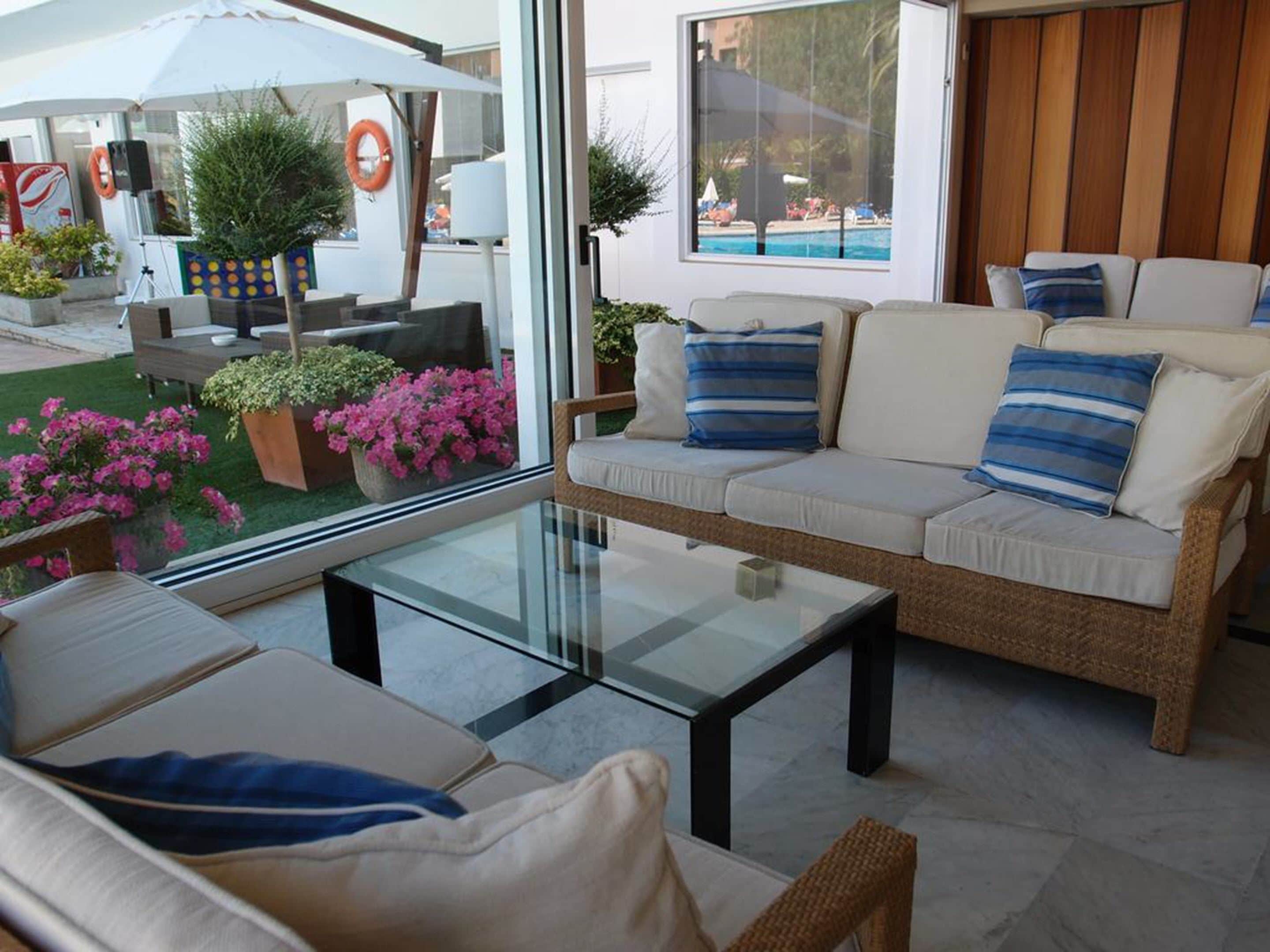 A modern living room with a glass coffee table, a sofa with striped pillows, and a view of a pool through large windows.