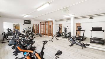 Une salle de sport équipée de divers appareils d’exercice, notamment des vélos d’appartement, des tapis de course et des appareils de musculation elliptique.
