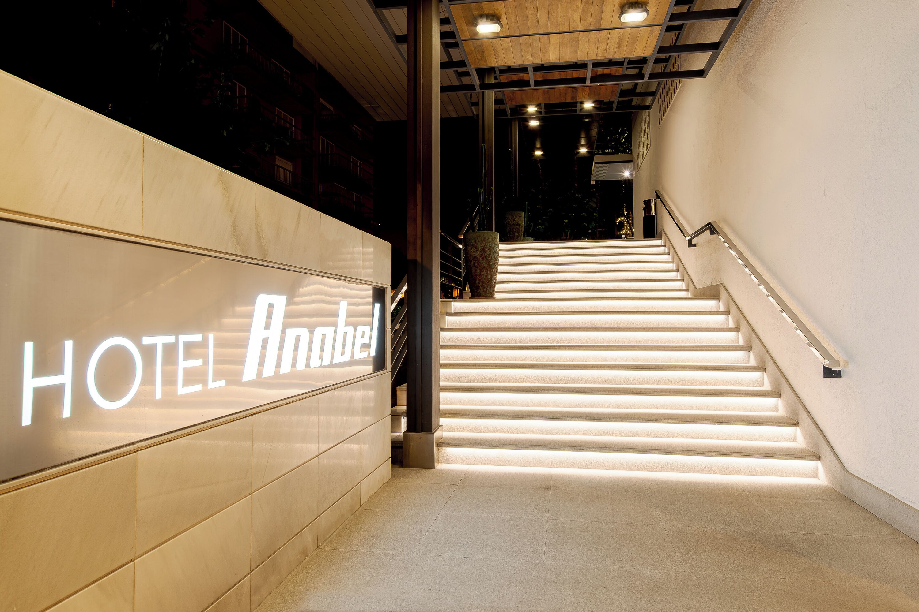 Entrada de un hotel con una escalera que conduce a los pisos superiores, un cartel que dice 'HOTEL Anabel' y un diseño interior moderno.
