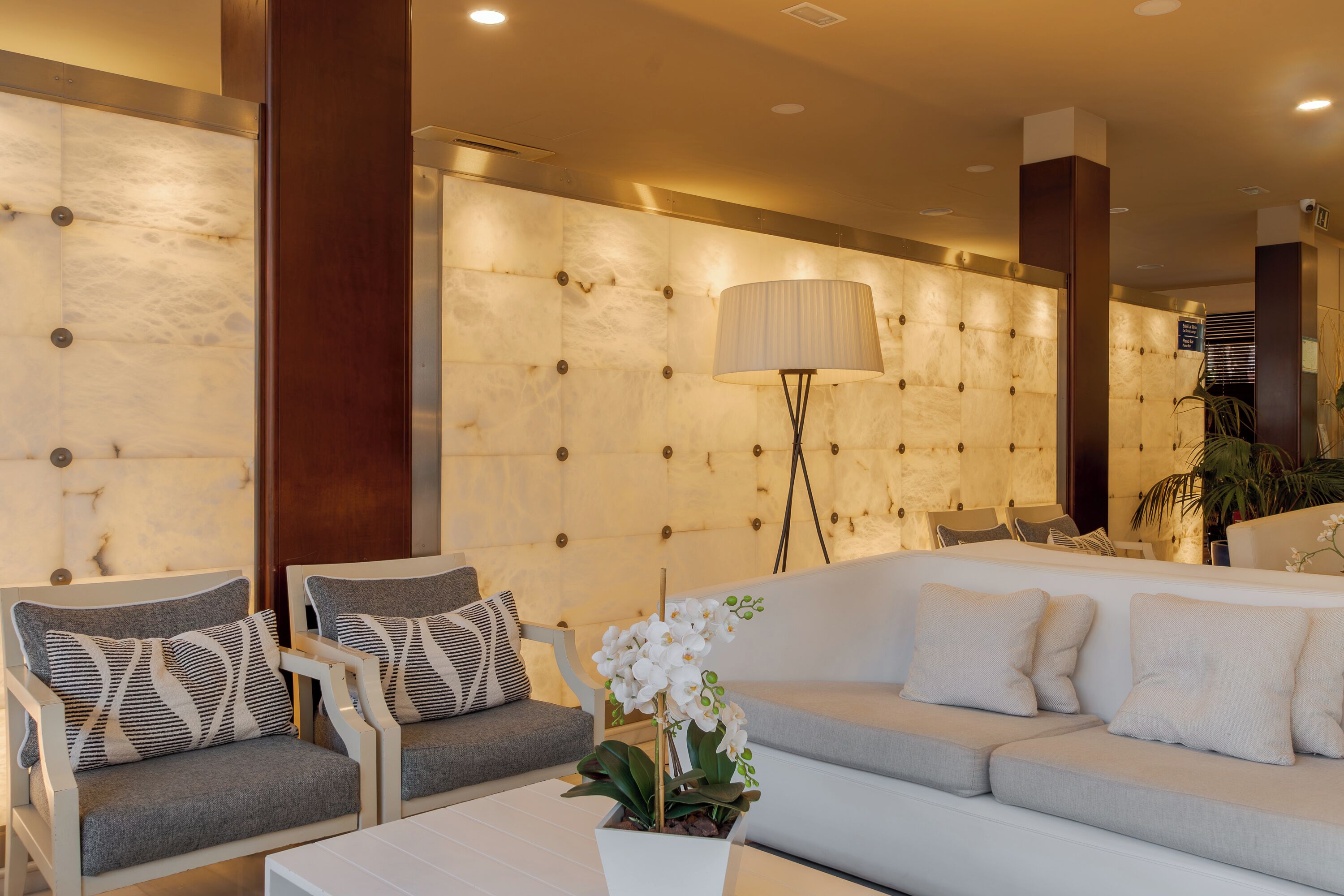 Un hall d’hôtel moderne doté d’un espace salon, d’un grand mur orné d’un motif capitonné et d’un lampadaire.