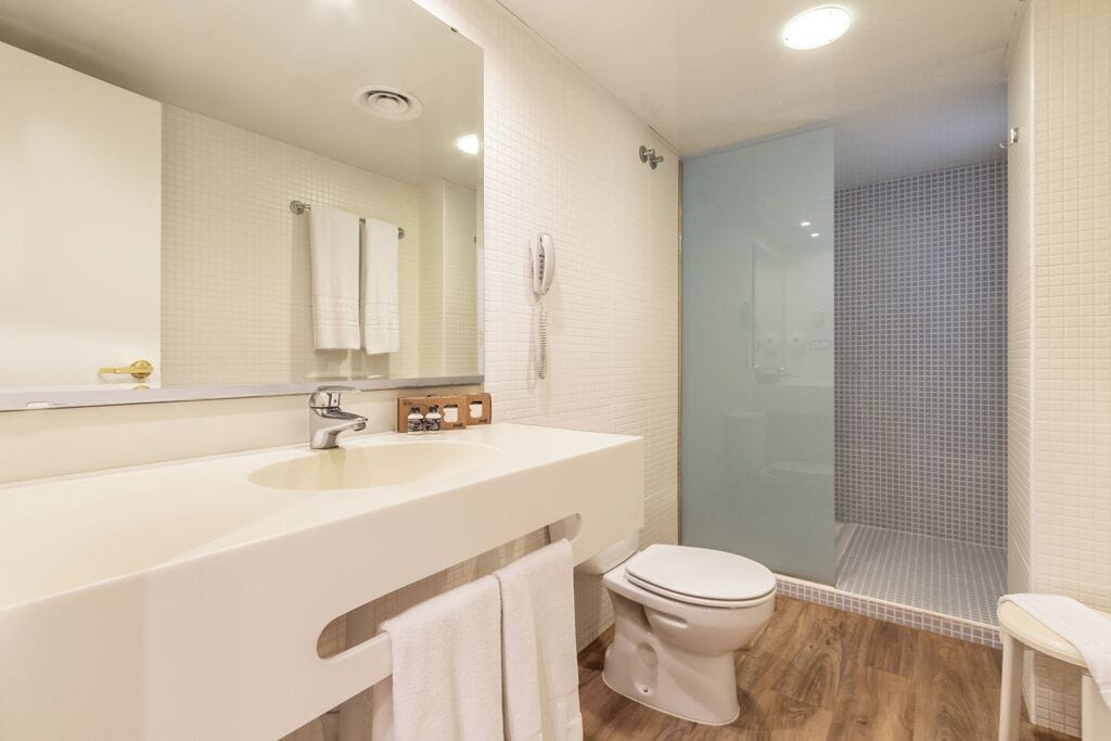 A modern bathroom with a large mirror, white sink, and a glass-enclosed shower.