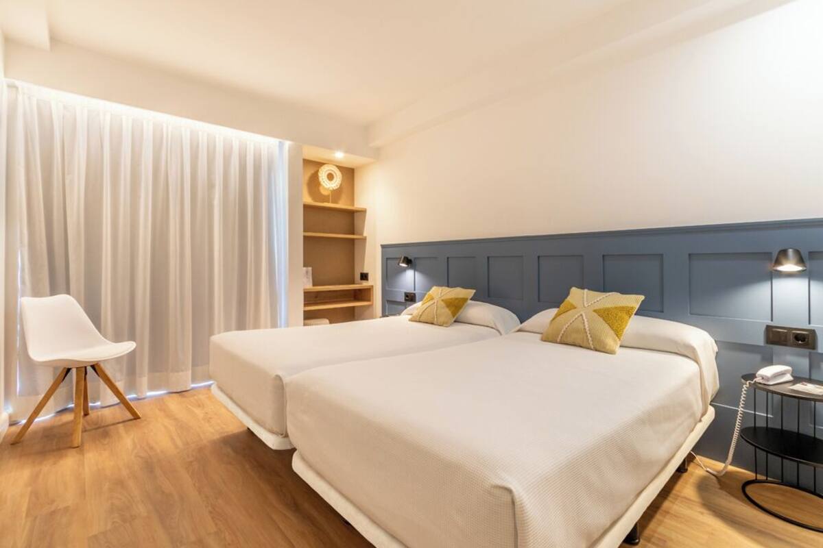 A hotel room with two beds, a chair, a desk, and a telephone.