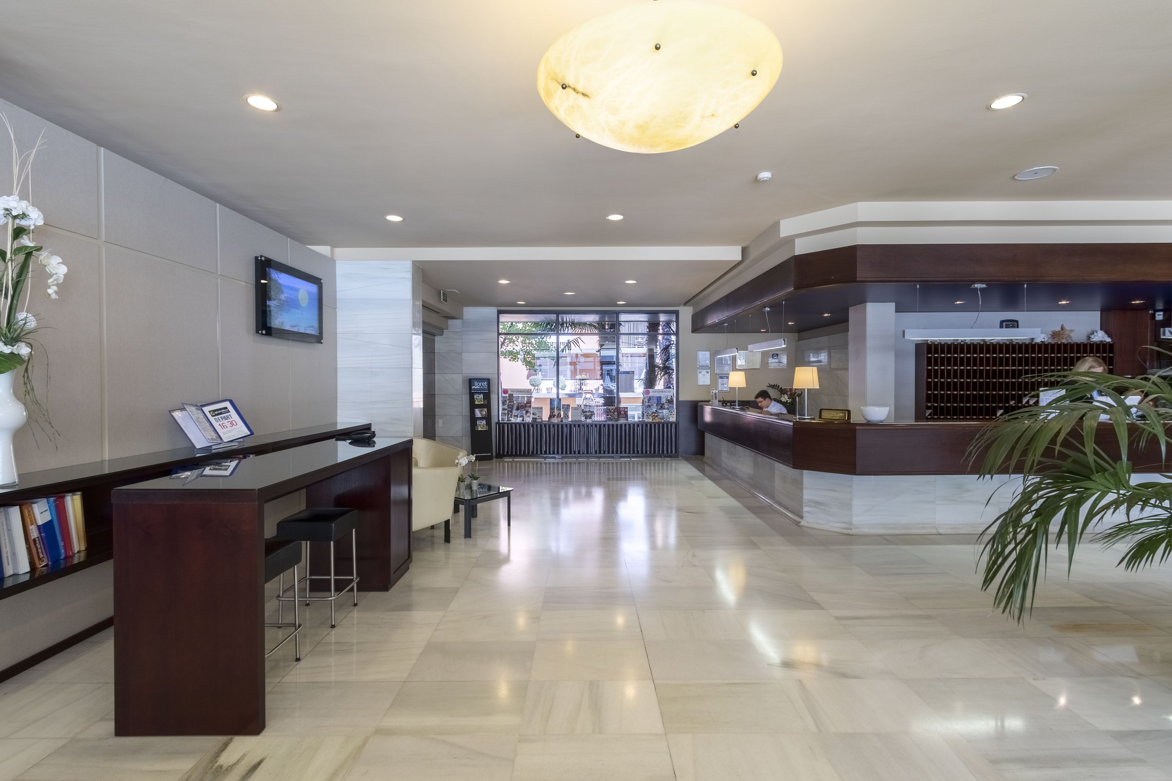 A modern hotel lobby with a reception desk, seating area, and a large chandelier.