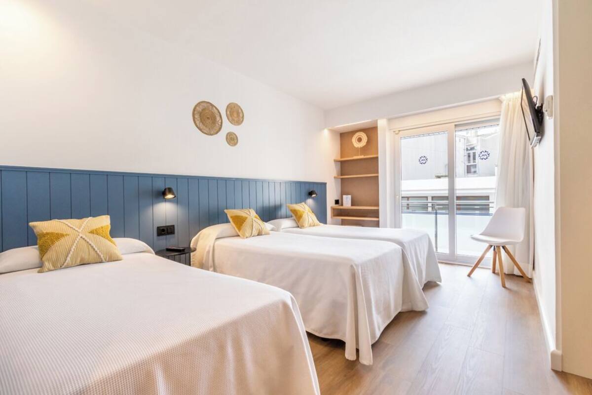 A hotel room with two beds, a blue accent wall, a balcony with a view, and a small seating area.