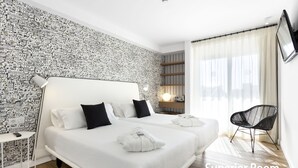 Habitación de hotel con una cama grande, una mesita auxiliar, una silla y una pared con un diseño de paisaje urbano.
