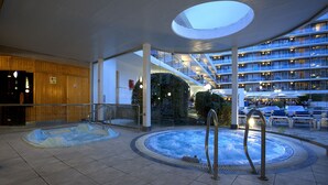 Vestíbulo de hotel con una amplia piscina interior, una escalera de cristal y vistas del exterior del edificio.