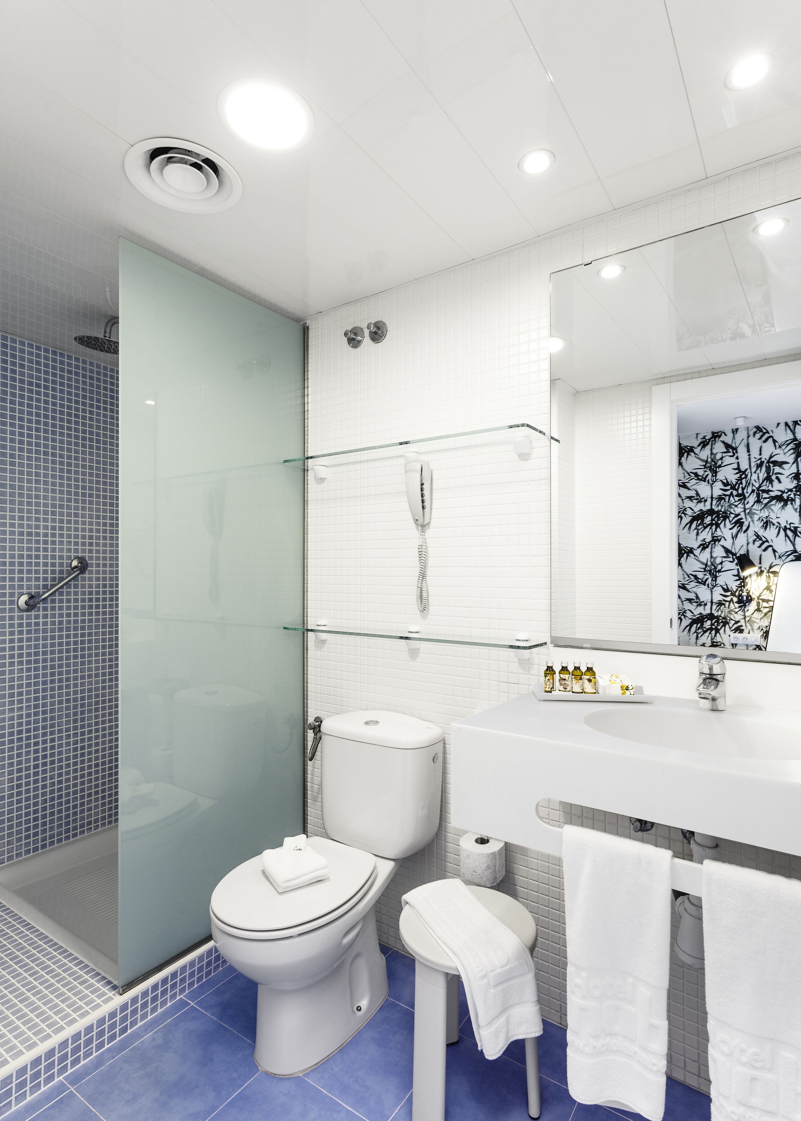 A modern bathroom with a glass shower enclosure, a white toilet, a sink with a mirror, and a glass shelf above the sink.