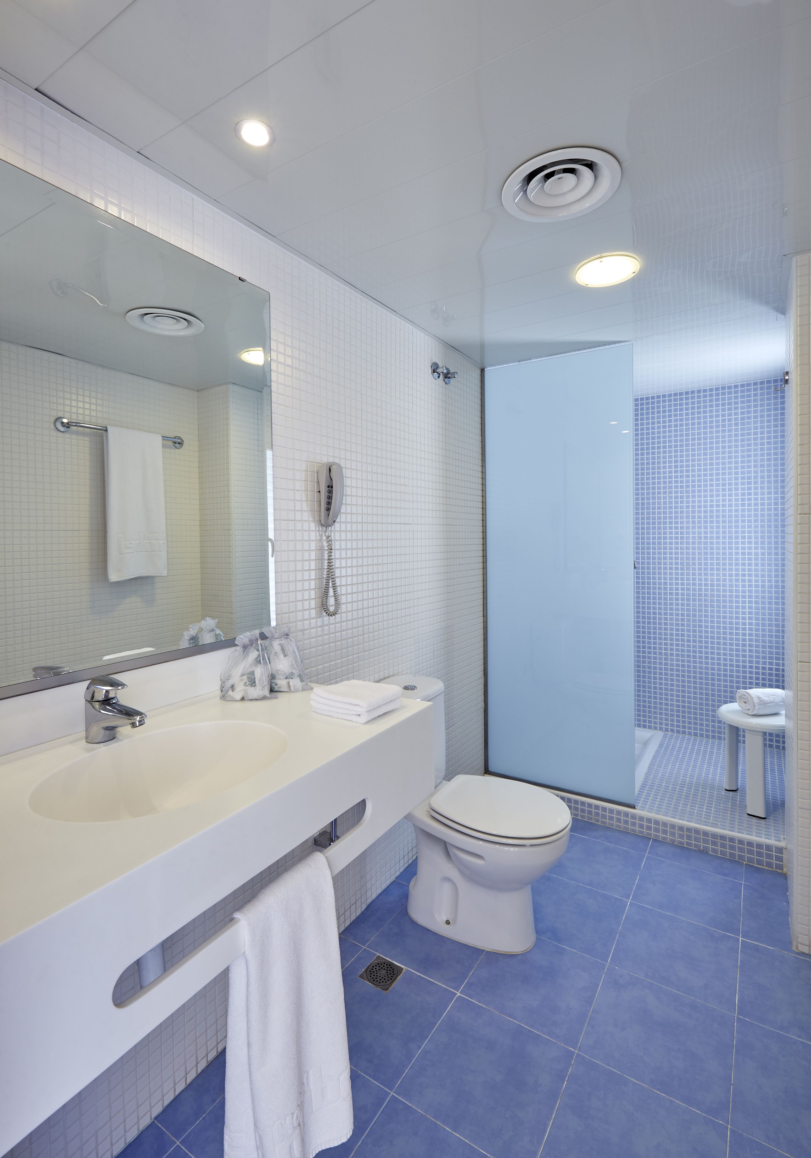 Een moderne badkamer met een grote spiegel, twee wastafels, een toilet en een douche met glazen wanden.