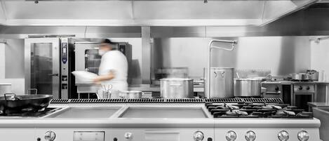 Una cocina comercial con electrodomésticos de acero inoxidable, incluyendo una estufa y un horno grandes, y un chef en movimiento.