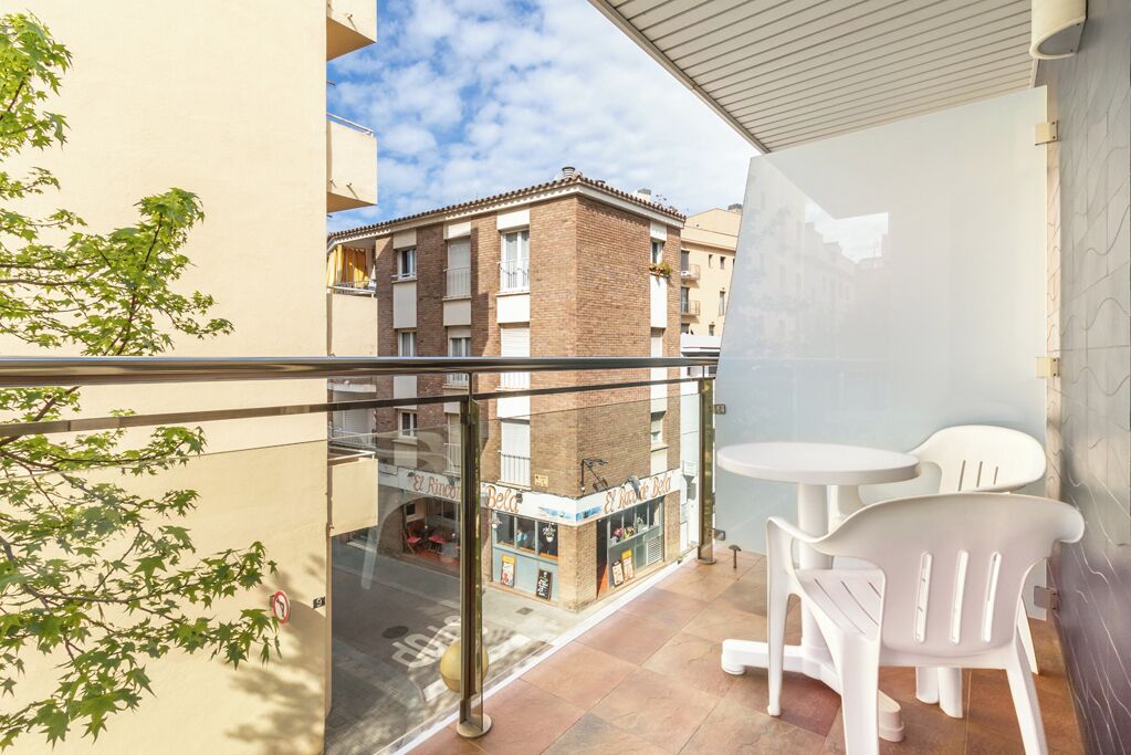 Un balcon doté d’une balustrade en verre, de deux chaises en plastique blanches et d’une petite table.