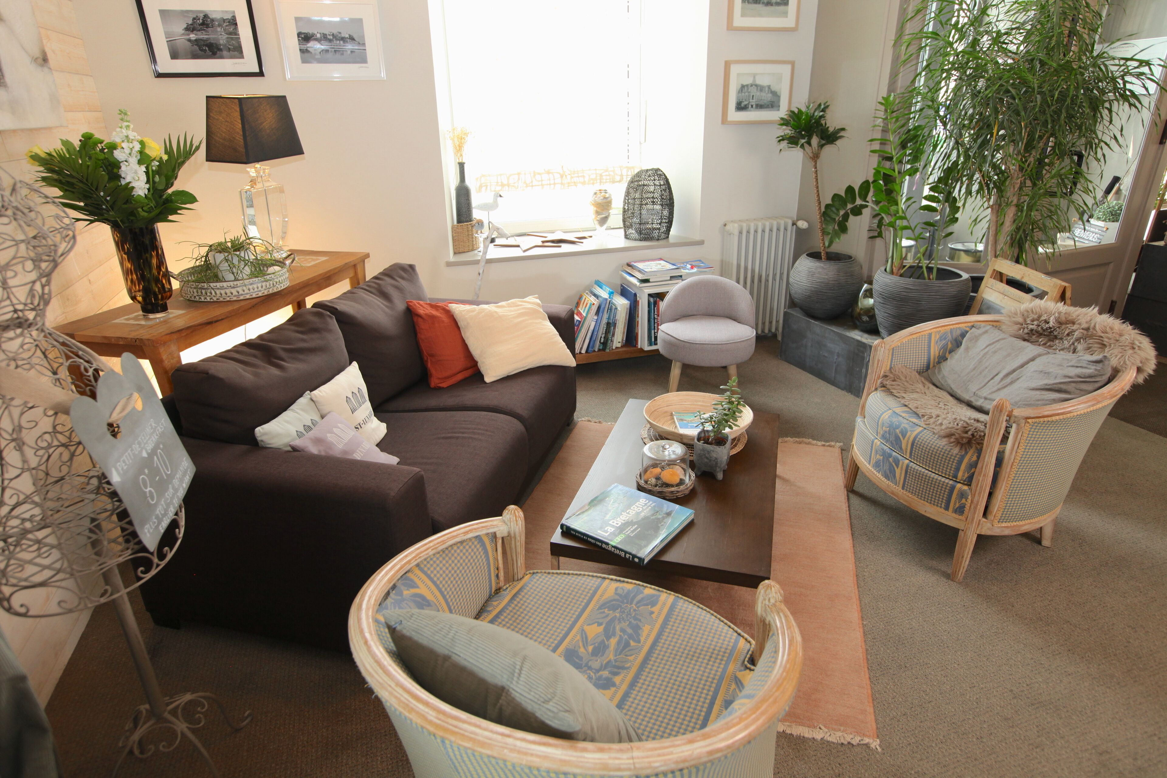 A cozy living room with a dark brown sofa, a wicker armchair, and a small round table with books and decorative items.