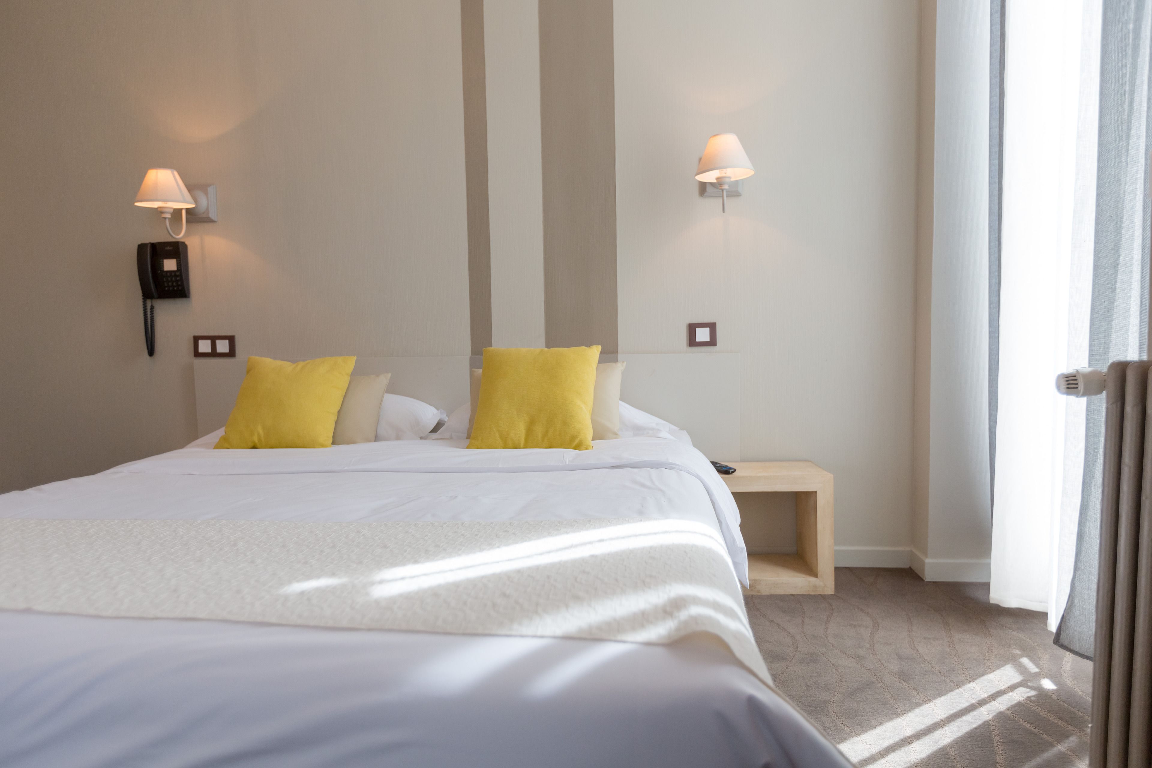 Habitación de hotel con una cama grande, dos lámparas de noche, un teléfono en la mesita de noche y una pequeña mesita de madera.