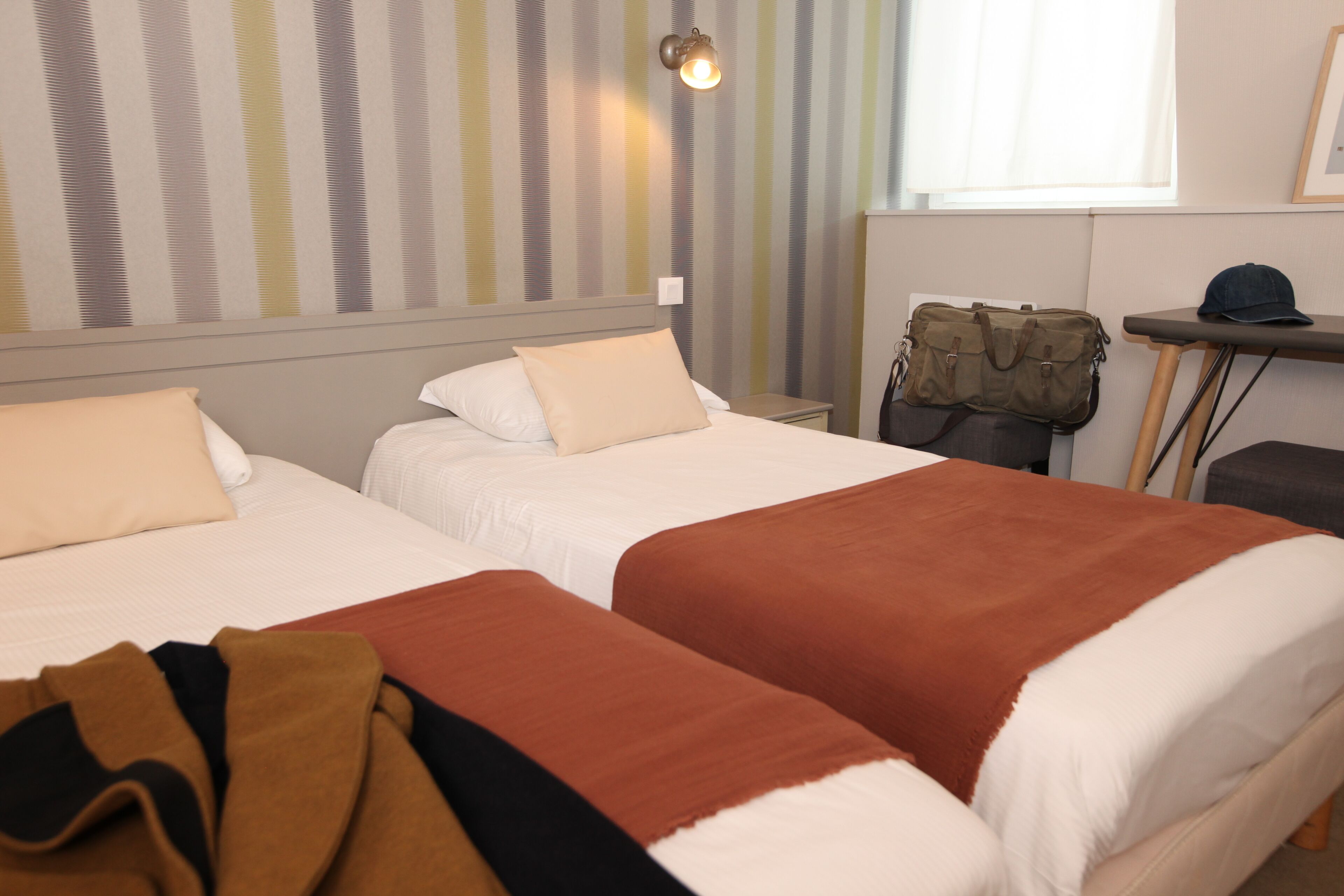 A hotel room with two beds, a desk, and a window.