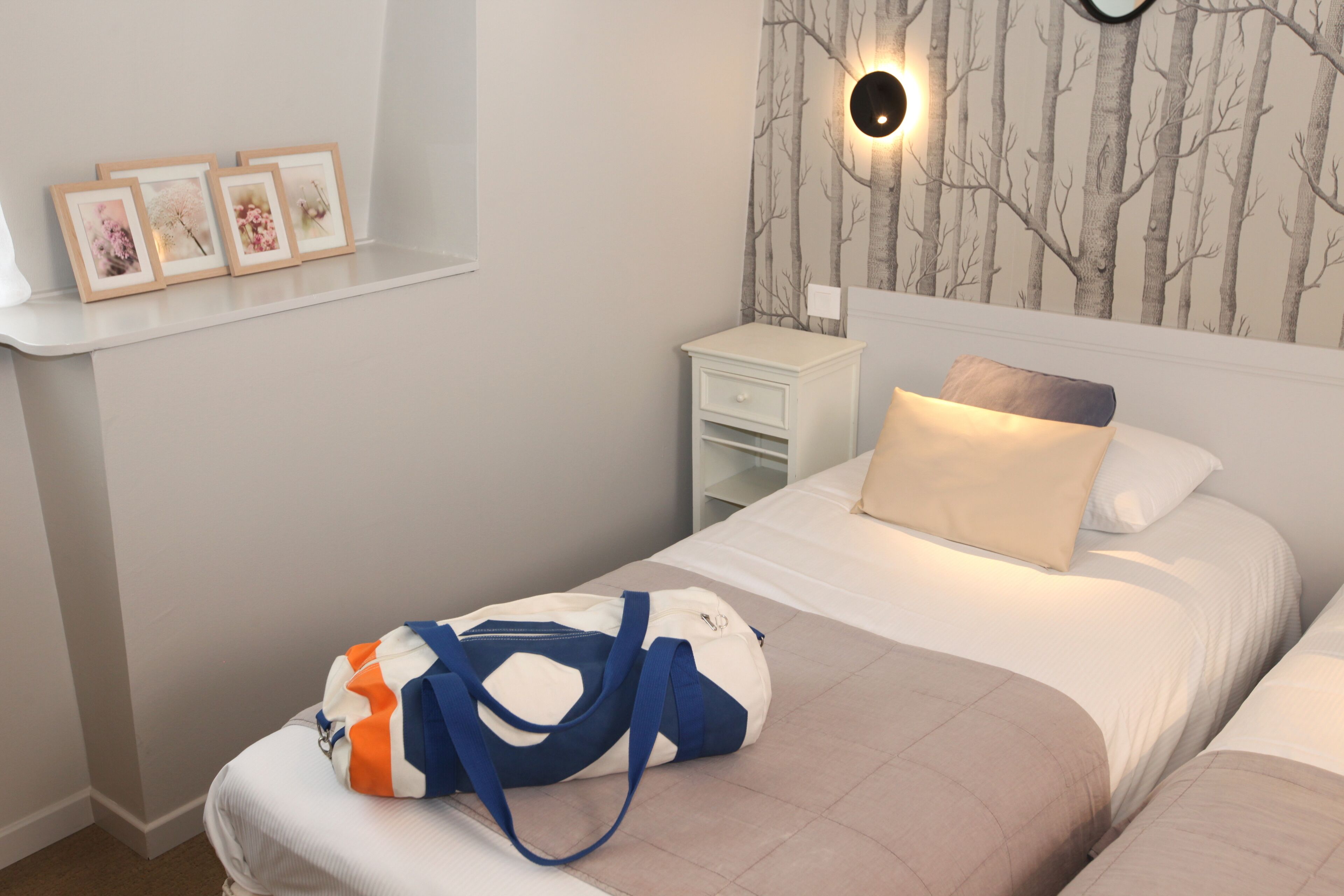 Een slaapkamer met een bed, een nachtkastje, een wandlamp en een plank met ingelijste foto's.