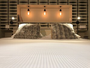 A modern bedroom with a large bed, patterned pillows, and a wall-mounted light fixture. - Citotel Les Alizes (Dinard)