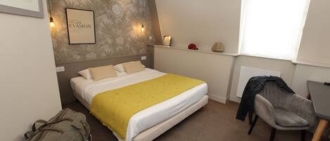 A bedroom with a bed, a desk, a chair, a backpack, and a wall with a framed picture and wall art.