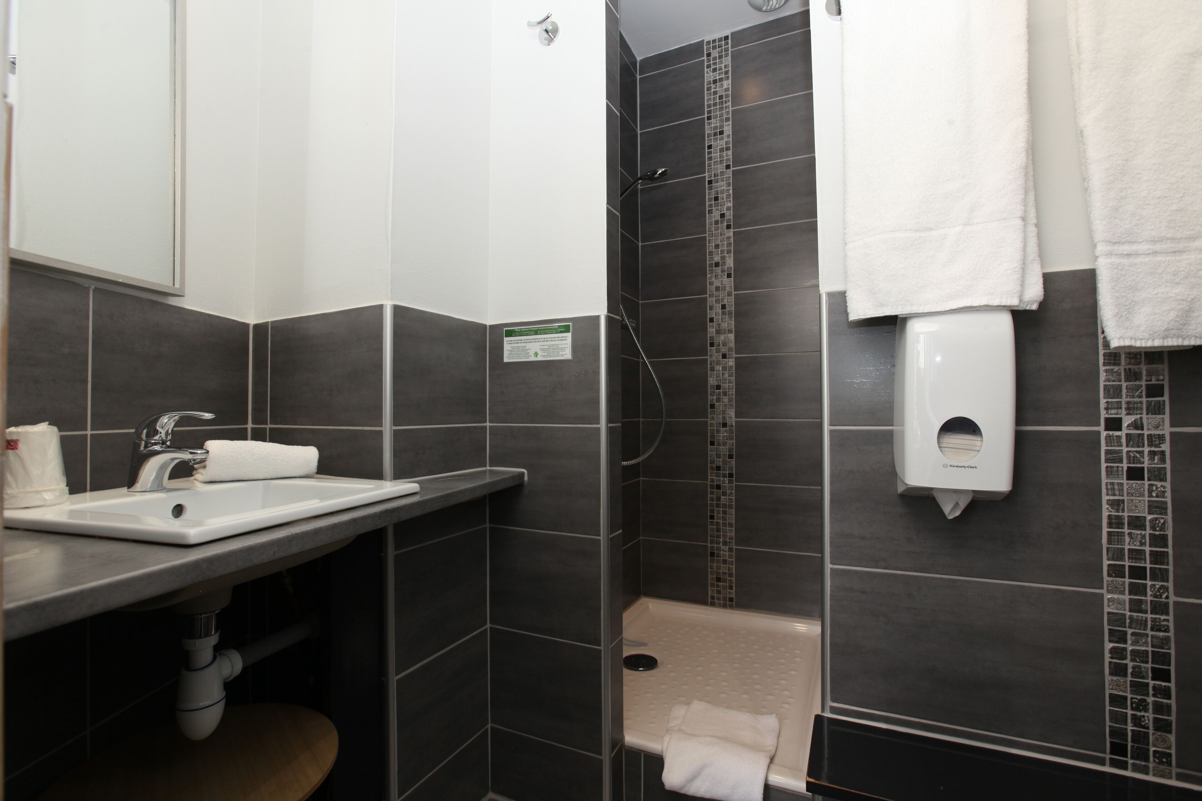 Un baño moderno con lavabo, espejo, dispensador de toallas y zona de ducha.