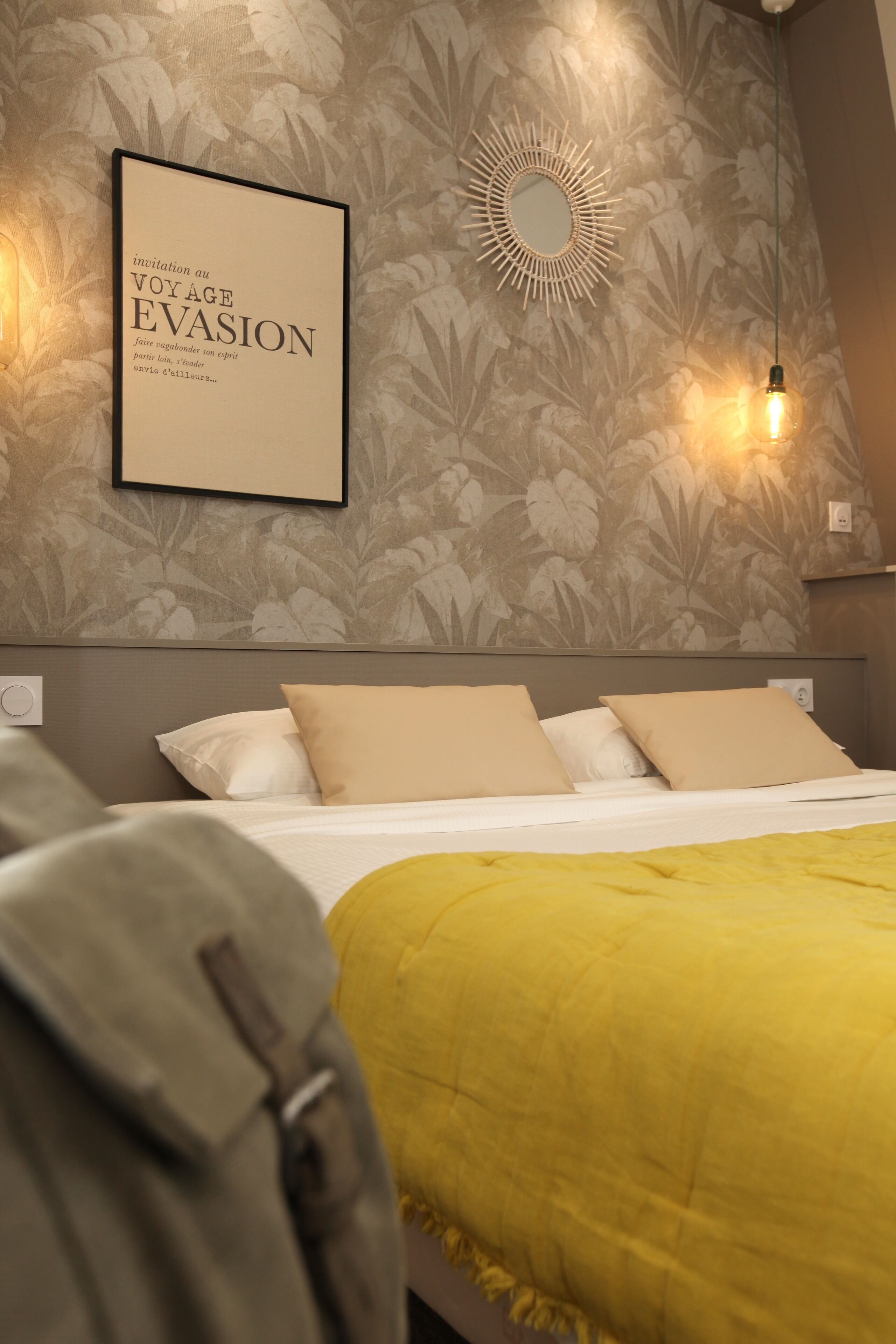 A bedroom with a bed, pillows, a yellow blanket, a wall-mounted mirror, and a framed text on the wall.