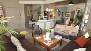 Sala de estar con sofá, sillones, una mesa de centro y una zona de cocina al fondo.