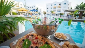 Una mesa junto a la piscina con una pizza, un bol de bebidas y una fuente de pasteles.