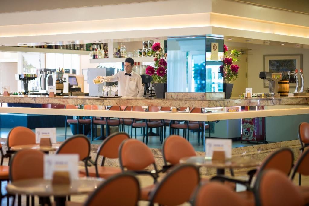A hotel bar area with a bartender, seating arrangements, and a counter with various items.