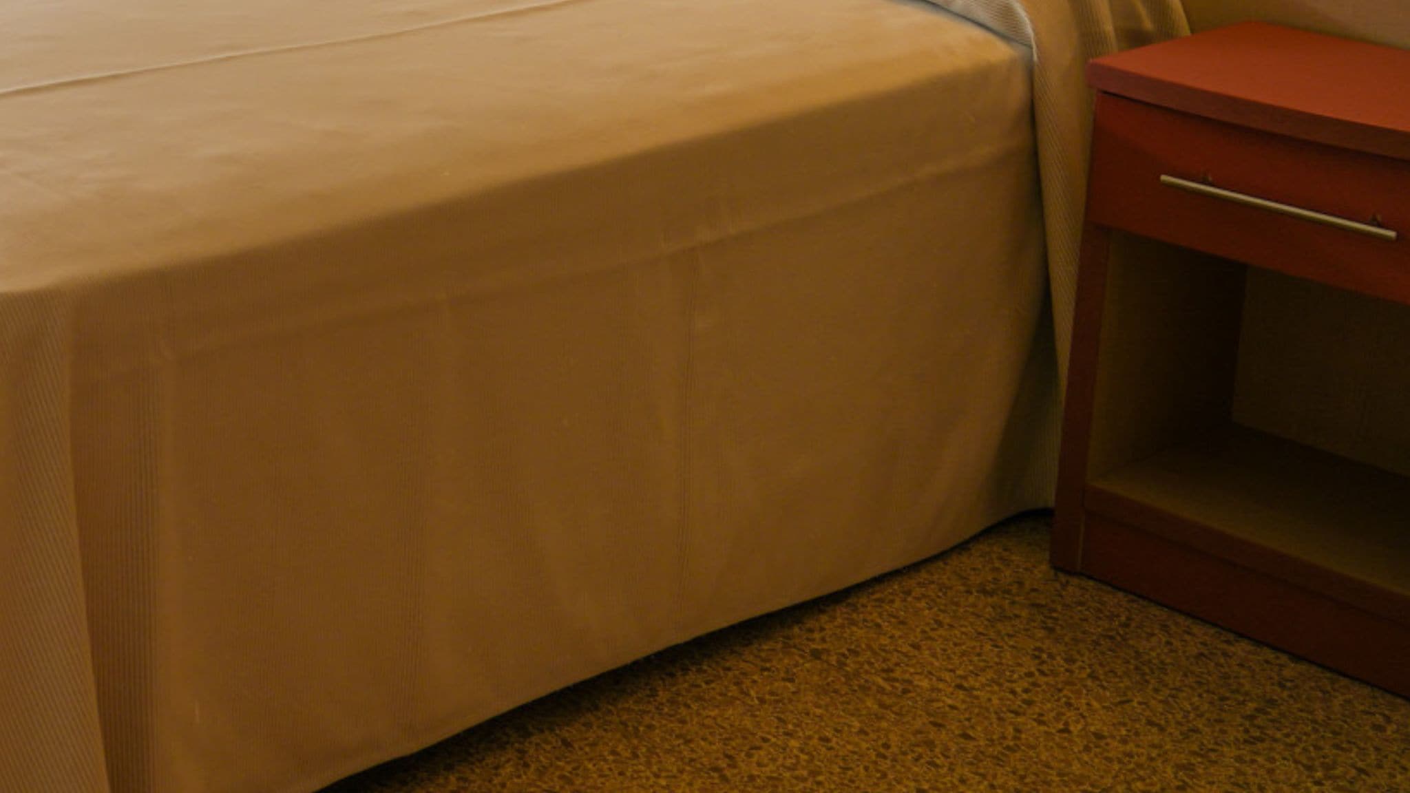 Una cama con colchón color beige y una mesita de noche de madera con cajón.