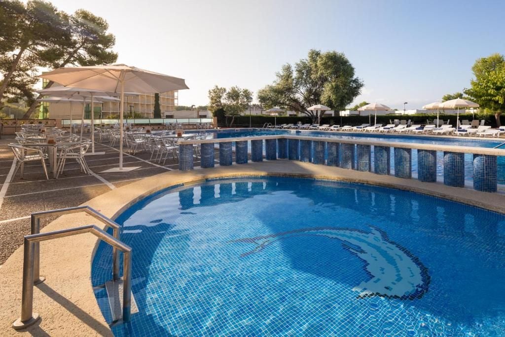 Piscina com borda azulejada, rodeada por espreguiçadeiras e guarda-sóis.