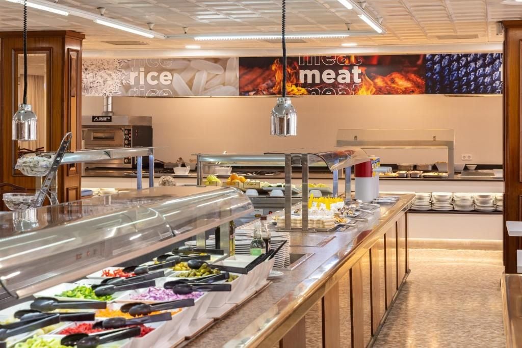 Zona de buffet con diversas opciones de comida, una estación de café y una pared con un anuncio de temática de fuego.