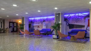 Un vestíbulo con diseño moderno, que presenta una zona de estar con sofás y sillones, una pared de mármol y una lámpara con forma geométrica.