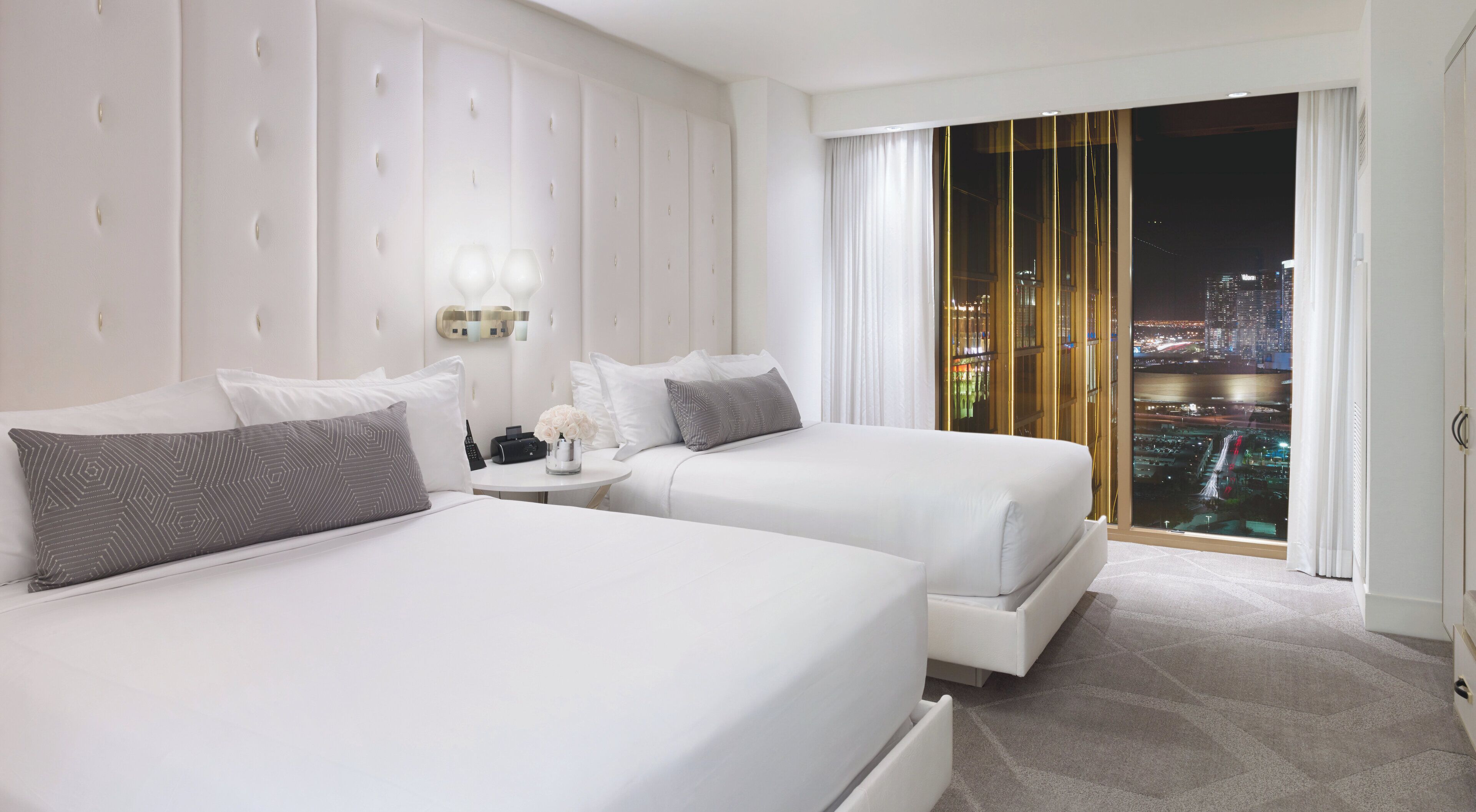 Hotelkamer met twee bedden, een nachtkastje en uitzicht op een verlichte stad.