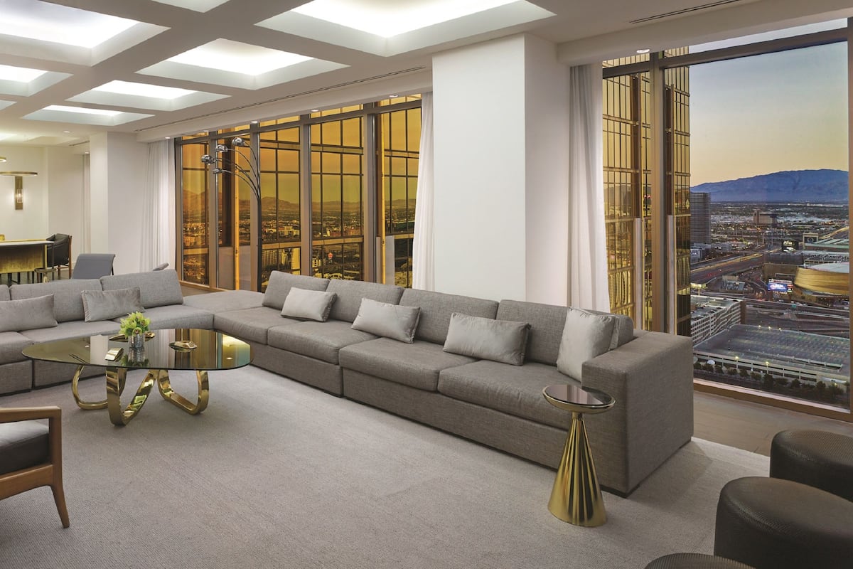 A modern living room with a sectional sofa, a glass coffee table, and a city view through large windows.