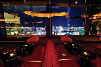 A modern dining area with a high ceiling, a city view, and a mix of yellow and brown upholstered chairs. at W Las Vegas
