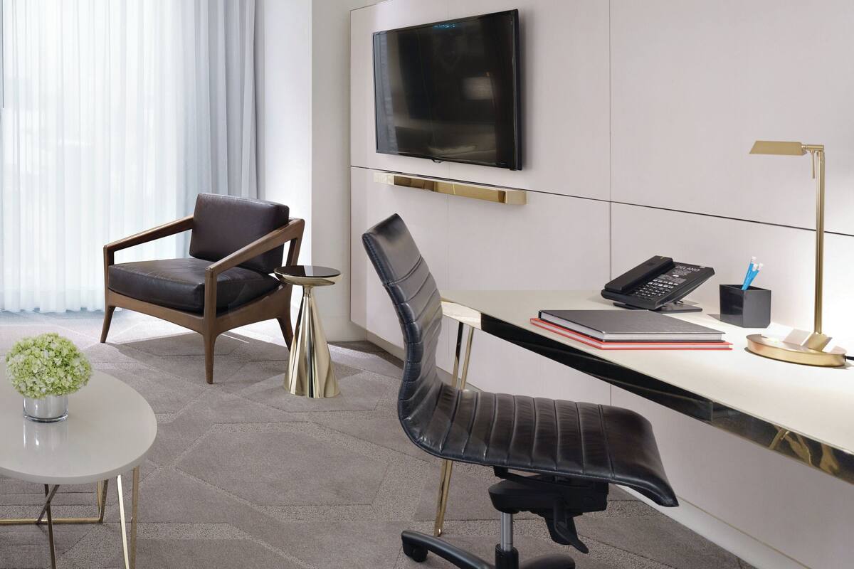 A modern office space with a desk, two chairs, a TV, a lamp, and a small table with a plant.