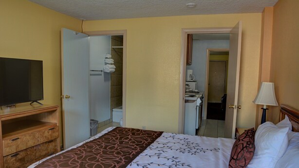 A hotel room with a bed, a TV on a wooden stand, a bathroom visible through an open door, and a lamp on the right side. - The Inn At Salmon Creek (Vancouver)