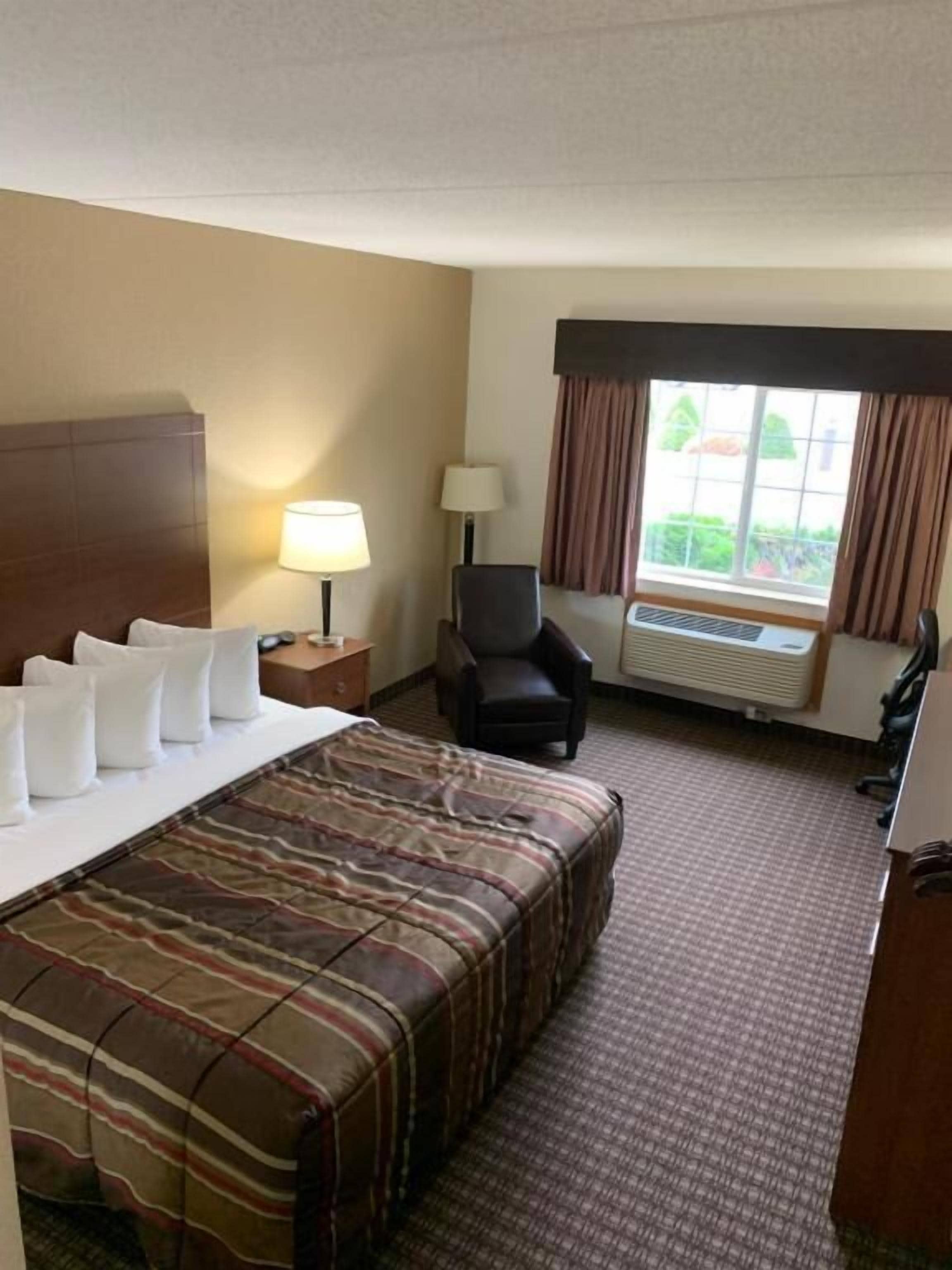 Une chambre d’hôtel comprenant un lit, deux tables de chevet, une chaise, un bureau et une fenêtre avec des rideaux.