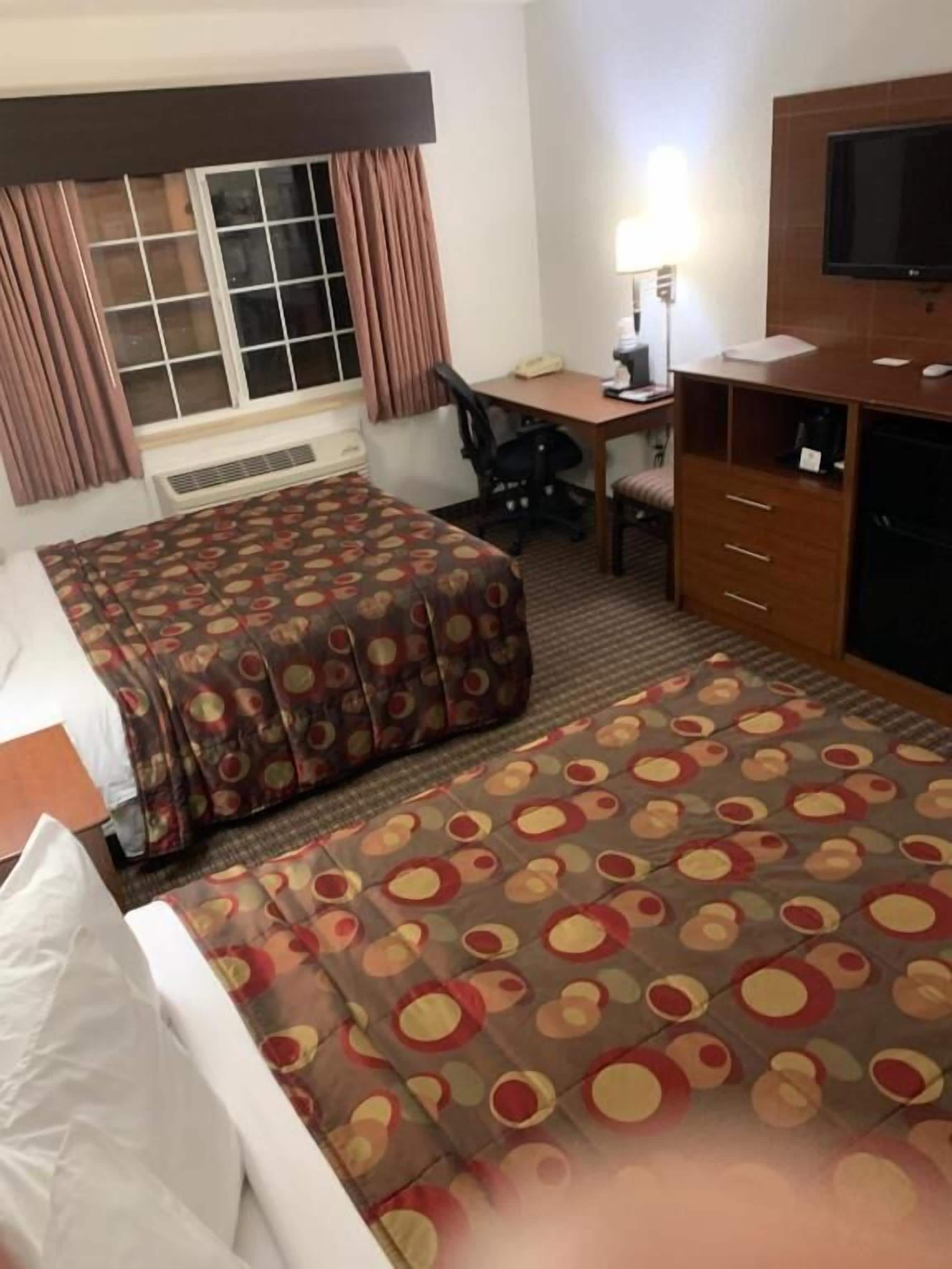 Habitación de hotel con dos camas, un escritorio, una silla, un televisor y una ventana con cortinas.