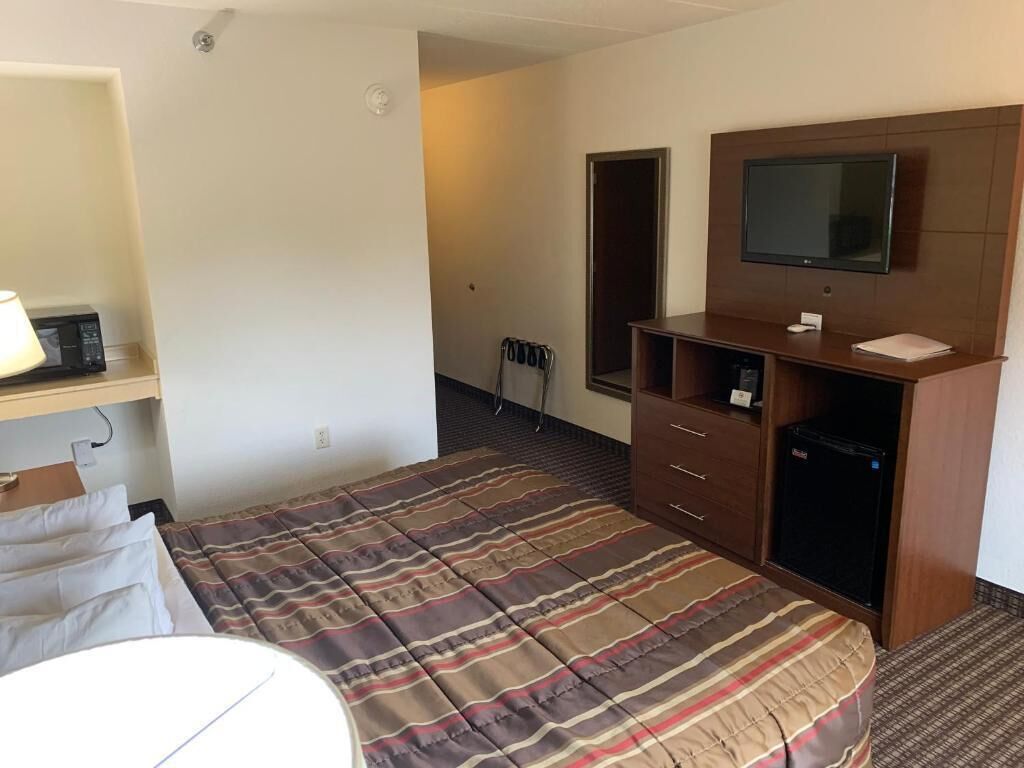 Habitación de hotel con una cama, televisión, escritorio y un refrigerador pequeño.