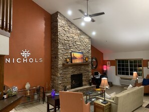 A modern living room with a stone fireplace, a ceiling fan, and a large window. - Nichols Inn of Red Wing (Red Wing)