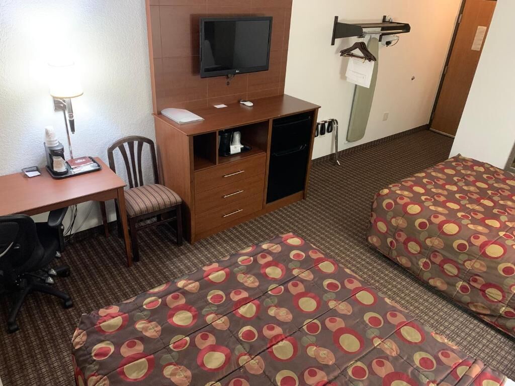 A hotel room with a desk, chair, television, and two beds with patterned bedding.
