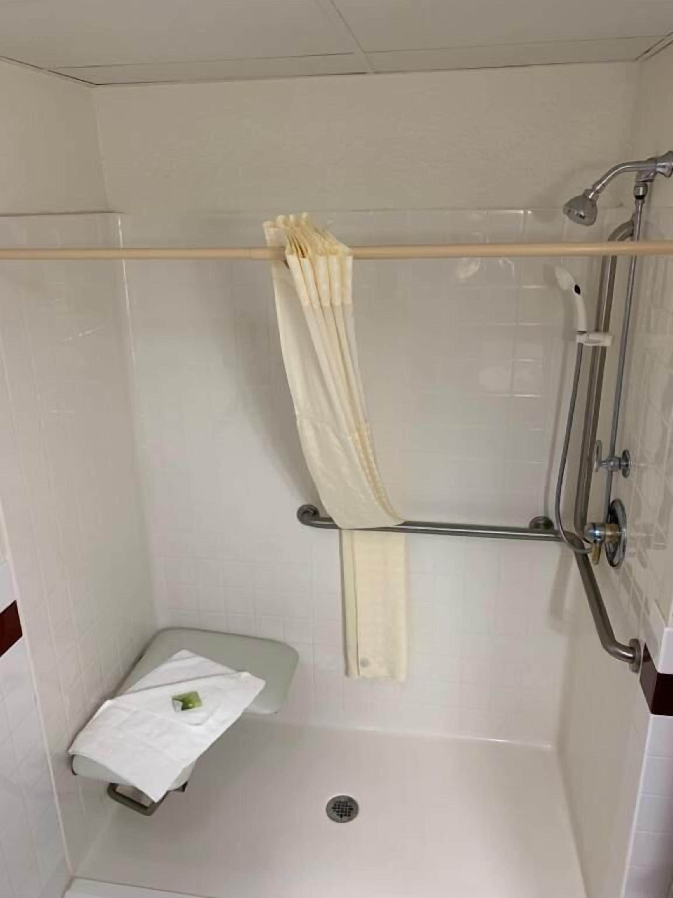 Un petit espace douche fermé, comprenant une pomme de douche, un porte-serviettes et un petit banc.