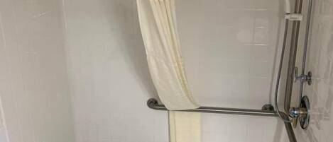 Un petit espace douche fermé, comprenant une pomme de douche, un porte-serviettes et un petit banc.