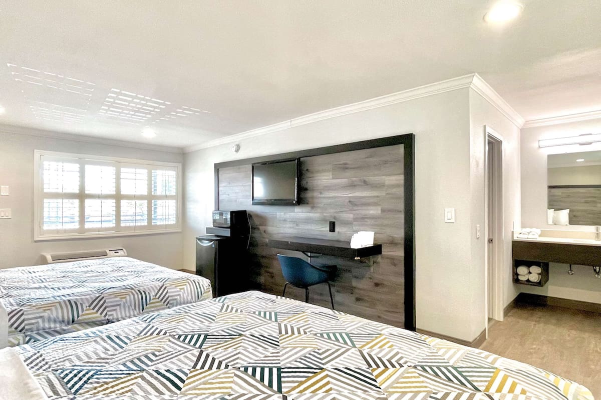A hotel room with two beds, a desk, a chair, a TV, and a mirror.